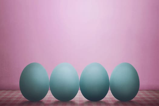 Row of easter eggs on desk against pink background
