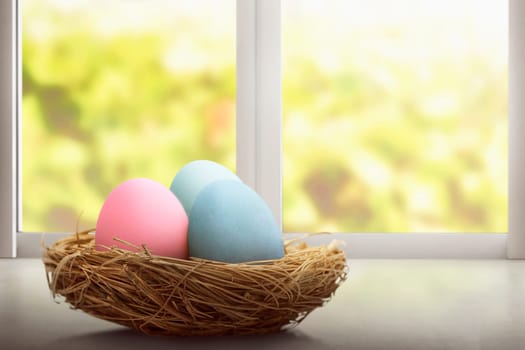 Colorful easter eggs in nest at desk in front of window background