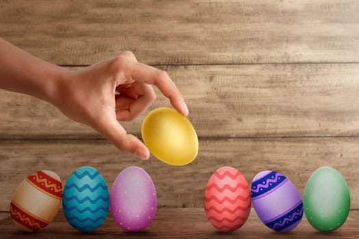 Hand put gold easter egg in row on desk with wooden wall background