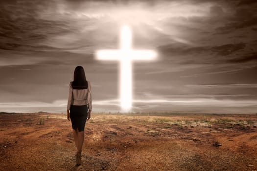Back view asian woman walking to bright cross shape on dry land background