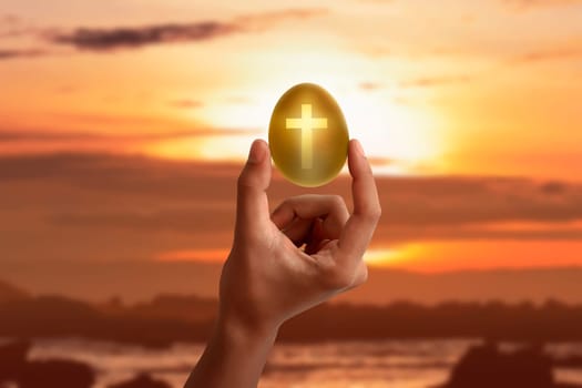 Hand holding the light of cross shape from the golden egg at sunset