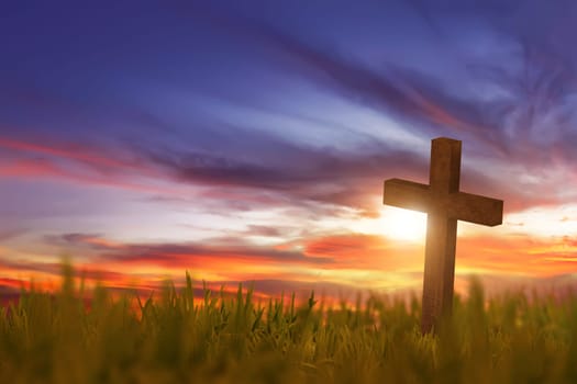 Wooden cross on green grass with sunset in the sky background