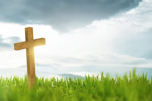 Wooden cross on green grass with white cloud background