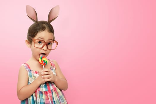 Smiling asian child girl wearing bunny ears on Easter day against pink background