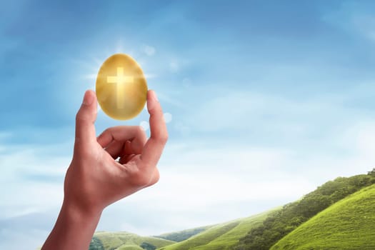 Hand holding the light of cross shape from the golden egg on the meadow