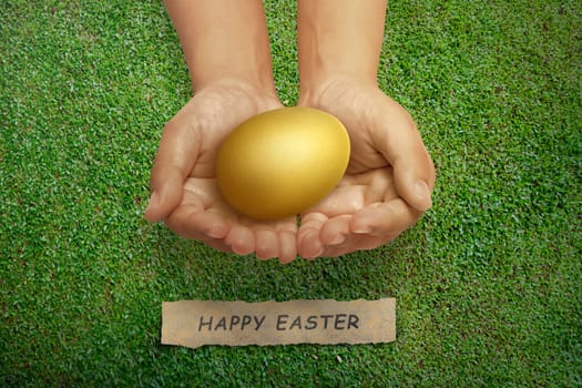 People hand holding gold easter egg with Happy easter greeting on green grass
