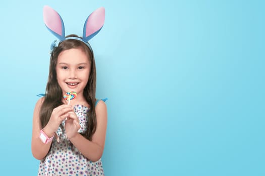 Happy asian little girl wearing bunny ears on easter day over blue background