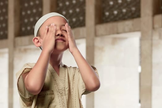 Cheerful asian muslim child praying to god in the mosque