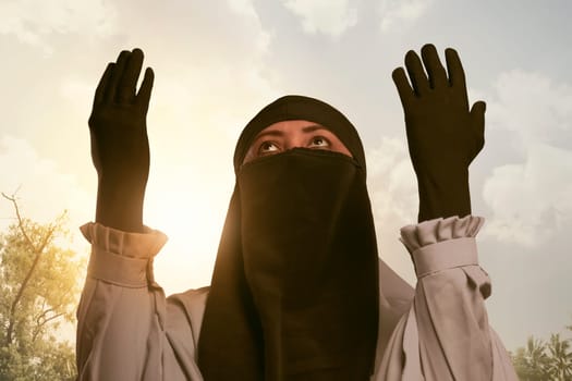 Beautiful asian muslim woman in traditional dress praying during sunset