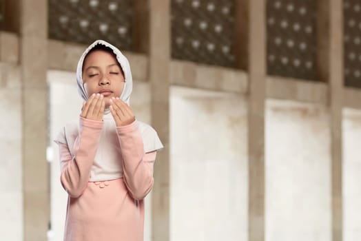 Asian muslim kid in hijab praying to god in the mosque