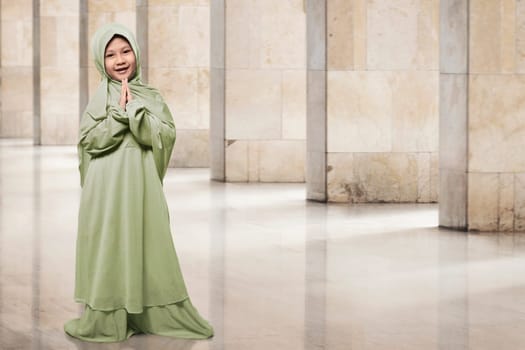 Asian muslim kid in green hijab clothes praying in the mosque