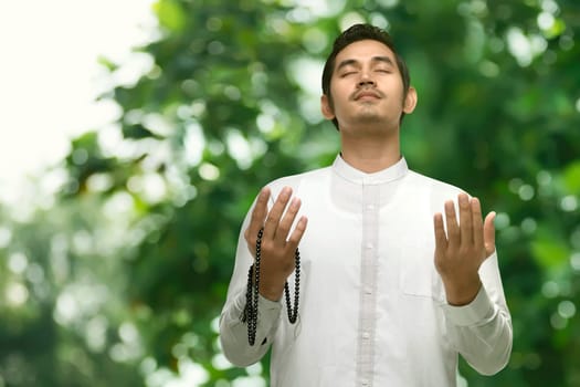 Young asian muslim man praying with prayer beads in the outdoor