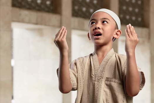 Little asian muslim boy is praying with raise hand in the mosque