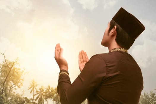 Devout asian muslim man praying with his both hands with sunset background