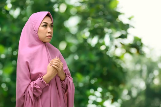 Pretty asian muslim woman in traditional dress praying to god with park background