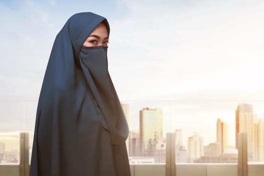 Religious asian muslim woman with covered face standing against cityscape background
