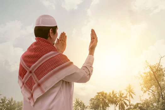 Back view of asian muslim man in white cap praying with sunlight background