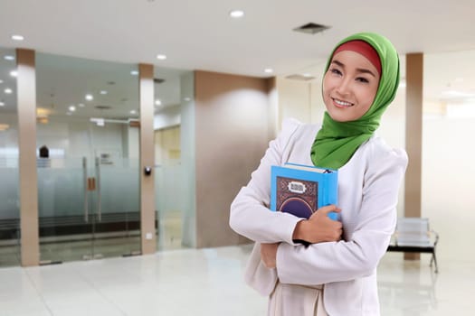 Young asian muslim woman in veil with koran standing at indoor