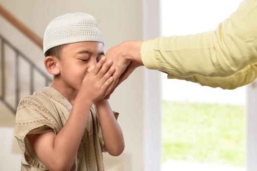 Little asian muslim boy with traditional dress kissing parents hand in the home