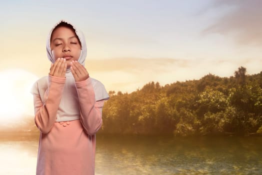 Pretty asian muslim child with hijab praying with scenics background