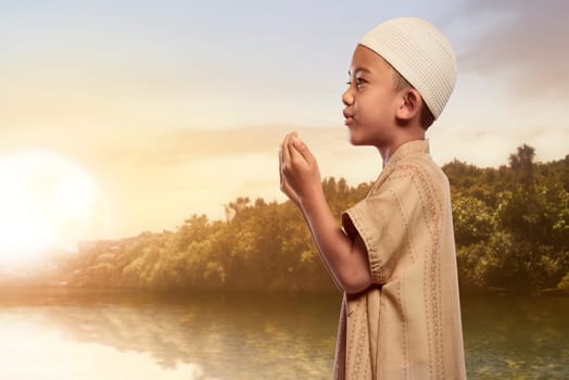Asian muslim boy with traditional dress praying at outdoor