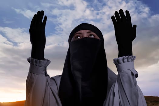 Religious asian muslim woman with hijab raising hand and praying against sky background