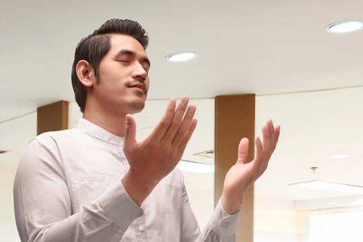 Young asian muslim man in traditional dress praying in the mosque