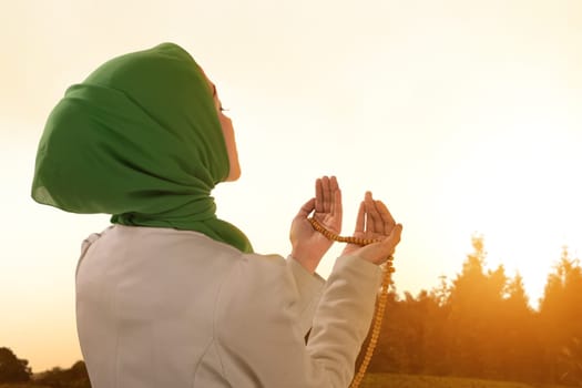 Beautiful asian muslim woman praying with prayer beads during sunset