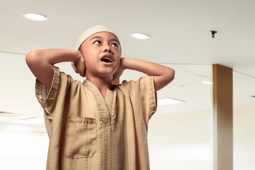 Religious asian muslim kid with cap praying in the mosque