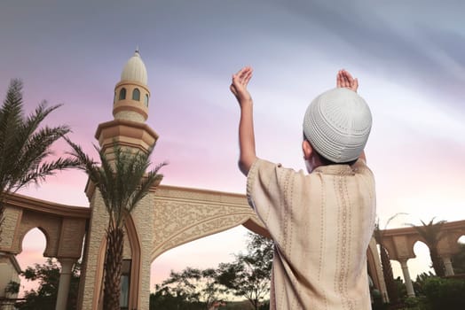 Rear view of asian muslim boy in traditional dress praying over sunset background