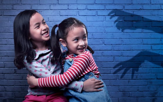 Scared two asian little girl looking at black ghost hand on wall background