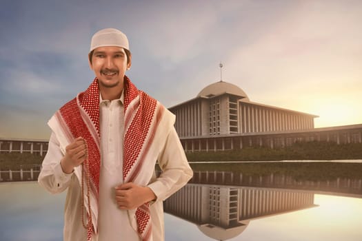 Handsome asian muslim man with traditional dress holding prayer beads against mosque background