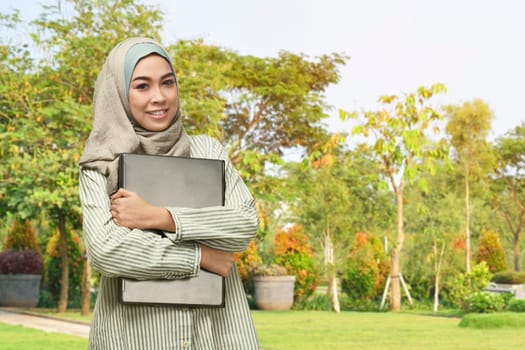 Beautiful asian muslim woman with smiley face holding laptop in the park