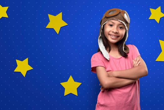 Funny asian little girl in astronaut costume standing over bright blue wall with yellow stars background