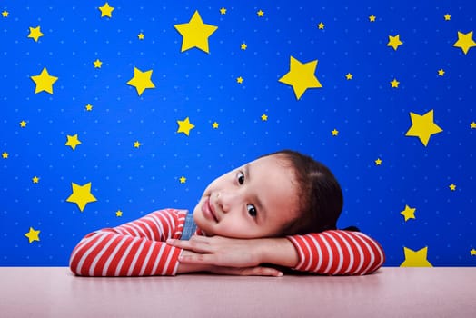 Smiling asian child resting on desk with yellow star on blue wall background