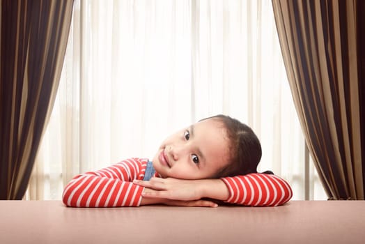 Smiling asian kid rests on the table at home