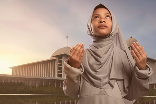 Pretty asian muslim girl in veil praying to god with mosque background