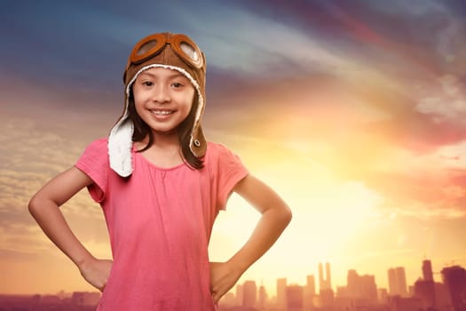 Funny asian kid with aviator hat dreaming of becoming a pilot against sunset at sky