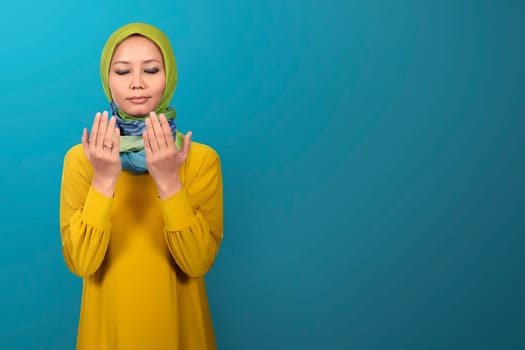 Beautiful asian muslim female praying against blue background
