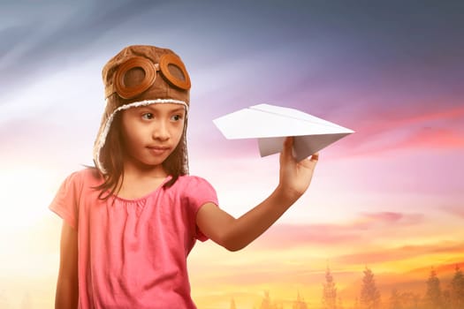 Happy asian child in aviator helmet playing with paper planes on the field