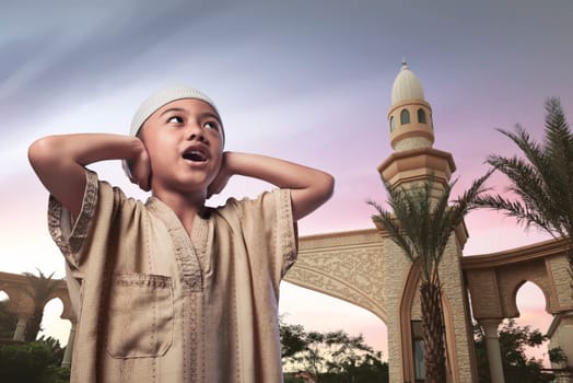 Asian muslim child with traditional dress praying against sky background