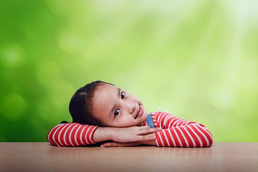 Cheerful asian kid lying down on the table over green background