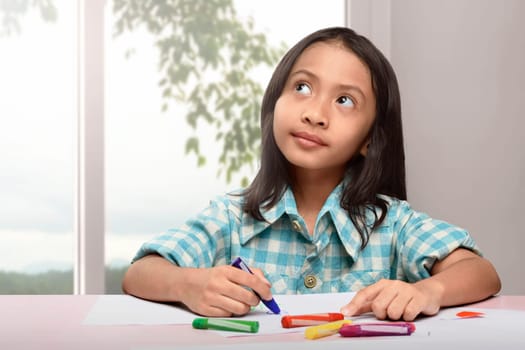 Cute asian little child drawing with colorful crayon at home