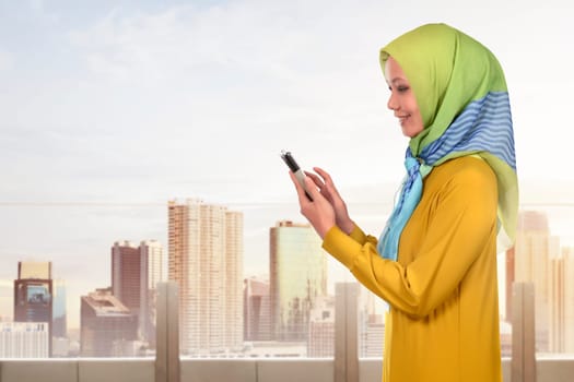 Asian muslim woman using smartphone while standing with cityscape background