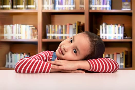 Beautiful asian little girl lying down on the desk resting at library