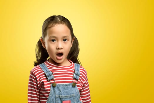 Portrait of asian kid with funny shocked face expression against yellow background