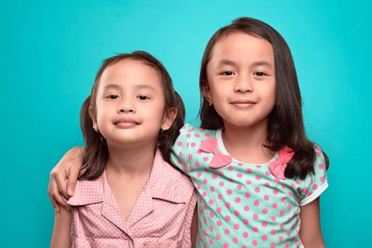 Happy two asian kids embracing and standing together against blue background