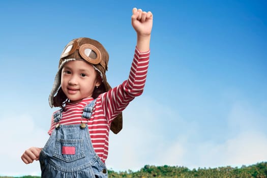 Funny asian little girl in aviator hat and goggles playing at field over blue sky background