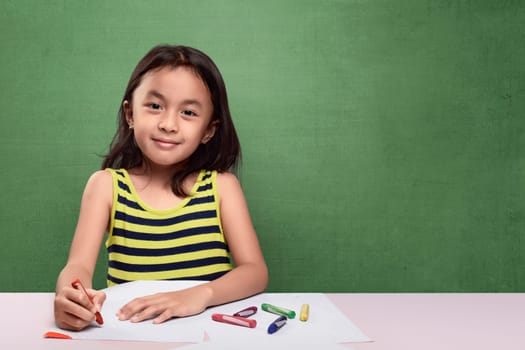 Portrait of asian kid drawing with colorful crayon against chalkboard background