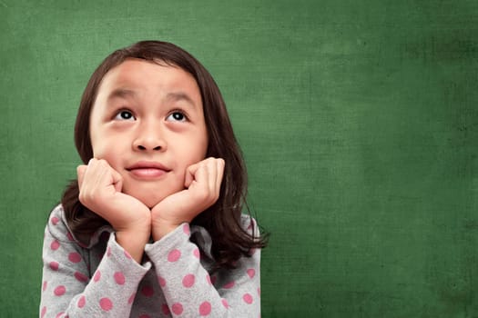Beautiful asian little girl with hands in chin imagine something against chalkboard background